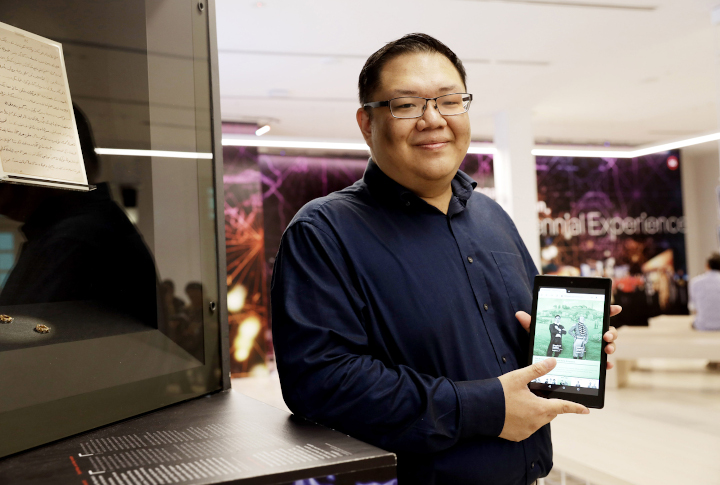 Joshua Sim, researcher for the Singapore Bicentennial Office, holds up an iPad showing a shot from the interactive book 700years.sg